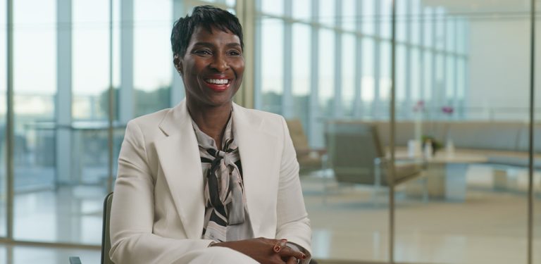 Sherrese smiling while seated in a bright office space with large windows. Photo courtesy of “Northwestern University Pritzker School of Law.”