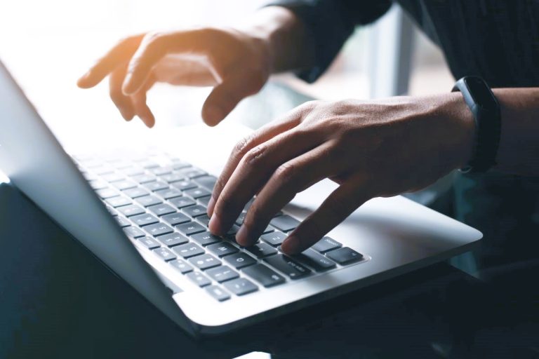 Close up of hands typing on a laptop keyboard while working on a computer.