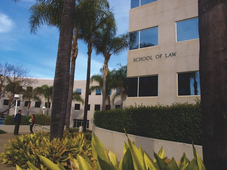UC Irvine School of Law building surrounded by palm trees and landscaping with “SCHOOL OF LAW” displayed on the exterior wall.