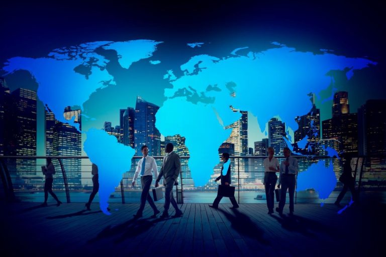 Silhouettes of business professionals walking in front of a glowing blue world map with a modern city skyline in the background.