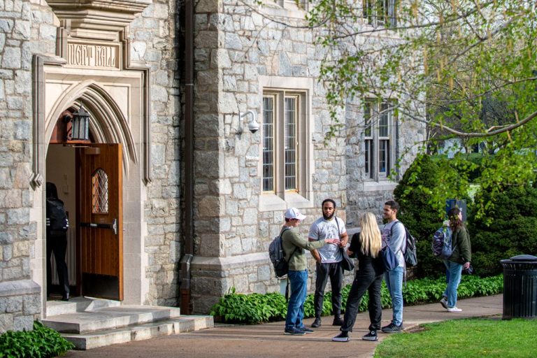 Students standing and talking outside Knight Hall at the University of Connecticut with the stone campus building and arched entrance behind them.