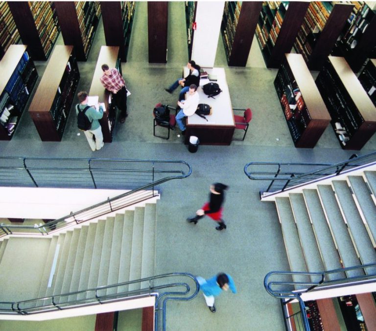 Overhead view of students studying and walking between bookshelves and tables inside a university library.