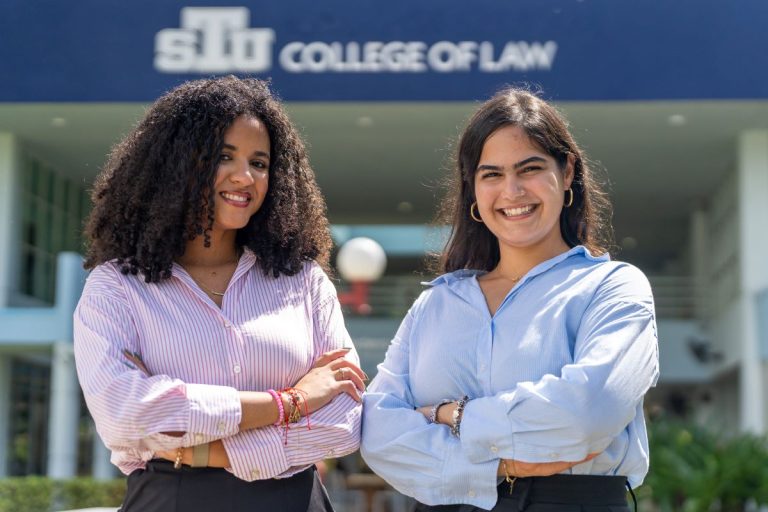 STU College of Law students Shanaya Chamizo and Camila Blanco smiling with arms crossed in front of the St. Thomas University College of Law building. Photo courtesy of “STU College of Law.”