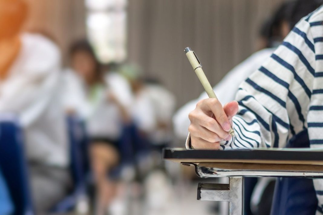 closeup of a hand holding a pen taking an exam in a room full of people