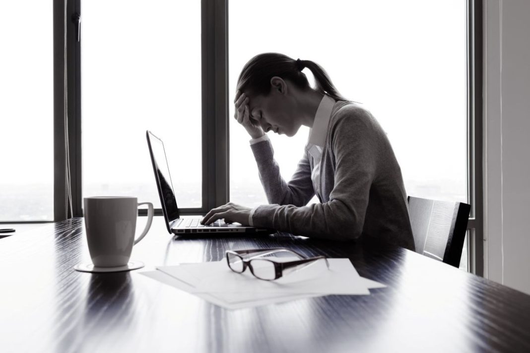 lady at table with a laptop holding her head with her hand