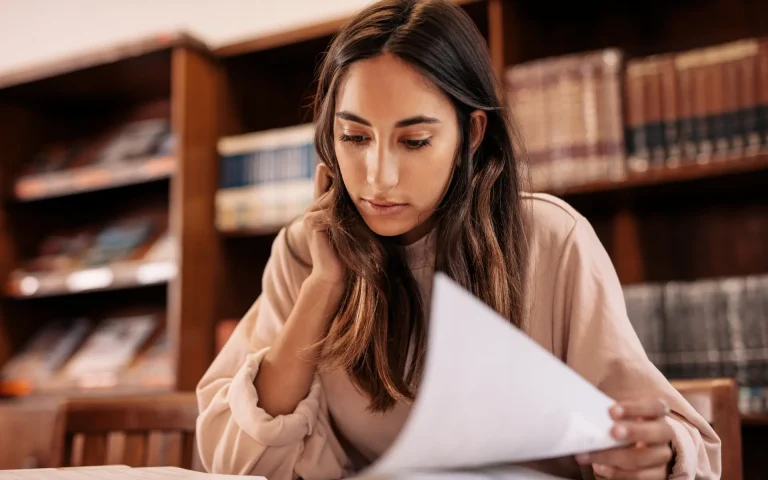 Young woman studying a document at a library table, with bookshelves filled with law books in the background.