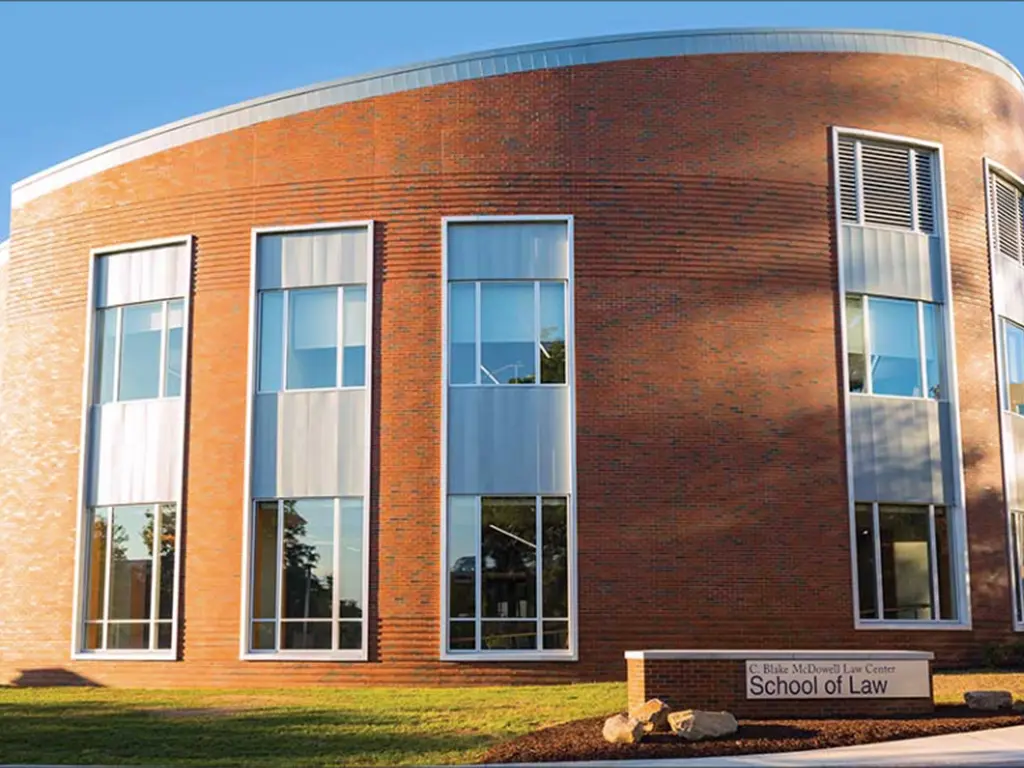 The C. Blake McDowell Law Center building, featuring a curved brick exterior with tall vertical windows and a sign reading “School of Law” on the lawn in front.