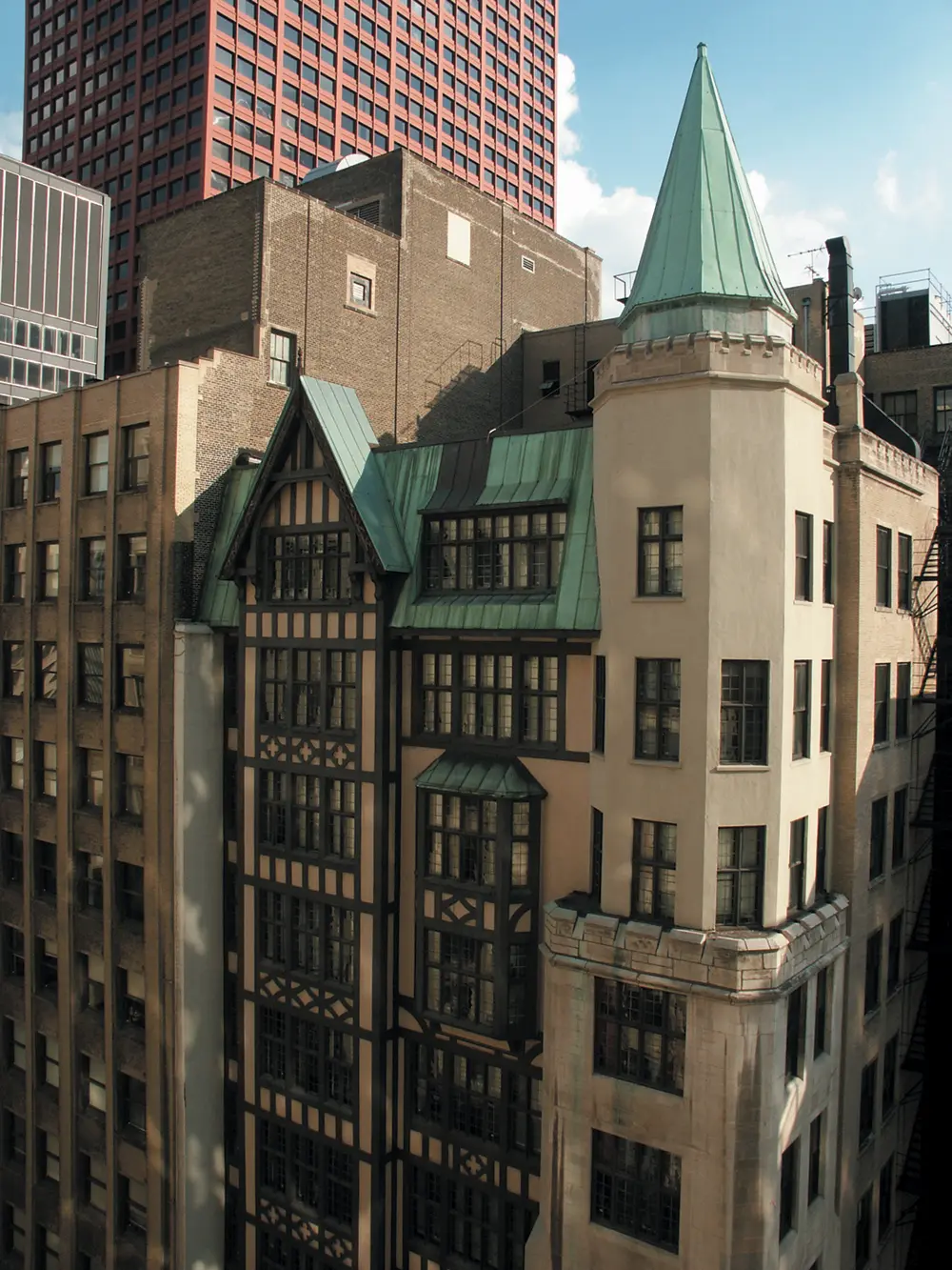 A detailed view of the DePaul University law building, featuring a historic-style facade with decorative half-timbering and green copper roofs, including a turret, set among taller modern city buildings.