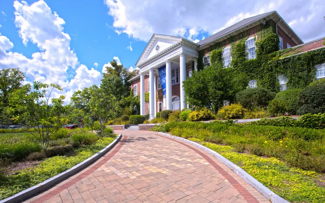 Brick university law school building with white columns and ivy-covered walls, viewed from a landscaped walkway leading to the entrance.