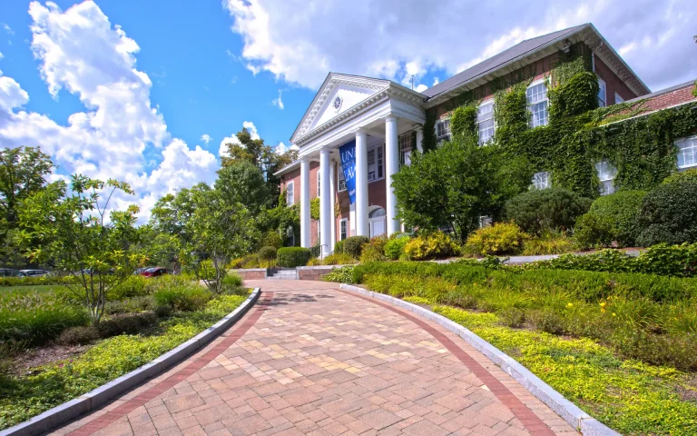 Brick university law school building with white columns and ivy-covered walls, viewed from a landscaped walkway leading to the entrance.