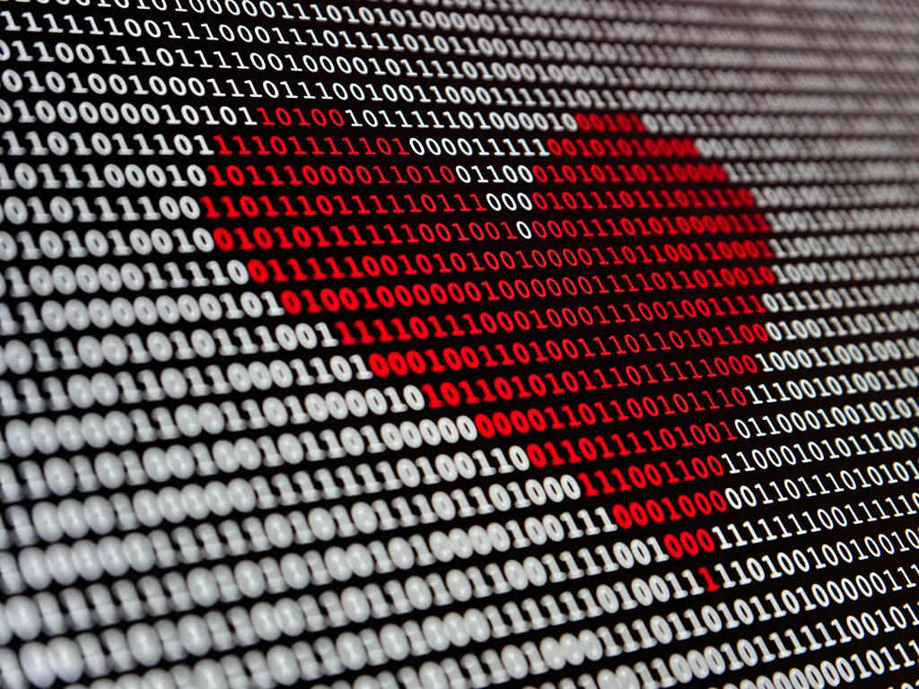 Close-up of binary code (0s and 1s) displayed on a screen, with a section highlighted in red forming a warning-like shape, symbolizing cybersecurity threats, hacking, or malicious code.