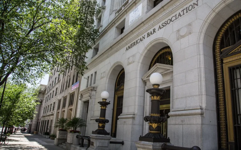 Exterior of the American Bar Association building with arched entrances, stone facade, and decorative street lamps along a tree-lined sidewalk.