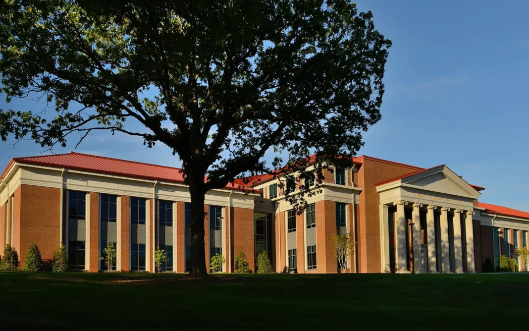 University of Mississippi Law School building with red brick architecture, white columns, and a large tree in the foreground on a grassy lawn.