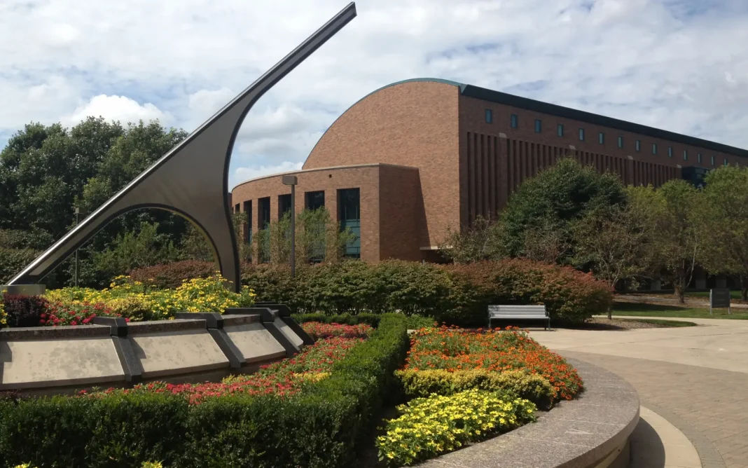 Drake University Law School building with a landscaped courtyard featuring colorful flower beds and a large curved metal sculpture in the foreground.