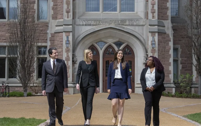 Four professionally dressed law students walking together and talking in front of Anheuser-Busch Hall on a university campus.