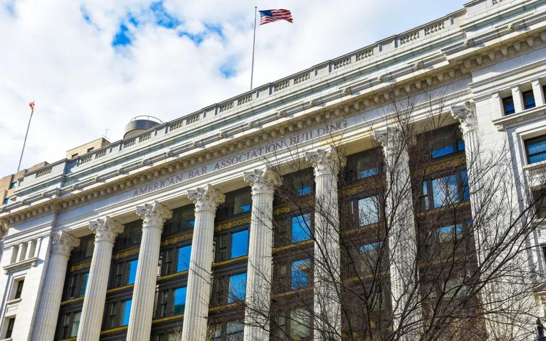 American Bar Association Building with tall classical columns and an American flag flying above the roof against a partly cloudy sky.
