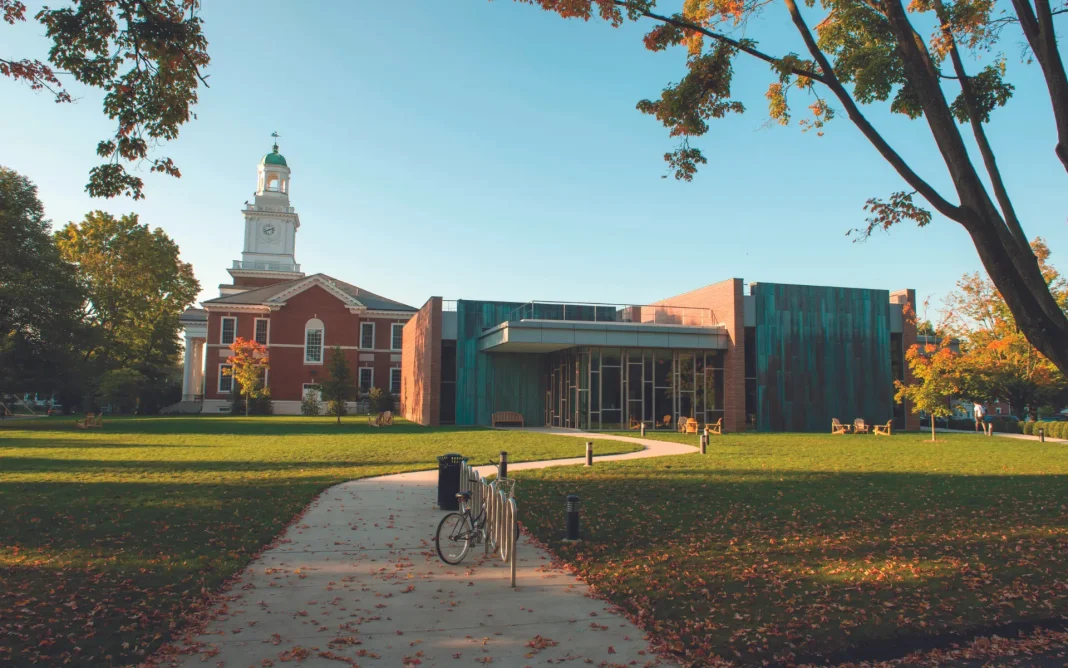 Penn State Law campus building with a modern glass-and-brick structure beside a historic red-brick building with a clock tower, surrounded by trees and a lawn with a walkway and bicycle rack.