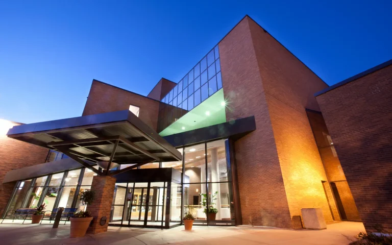 Modern red-brick law school building with large glass windows and a covered entrance canopy, illuminated at dusk against a clear blue sky.