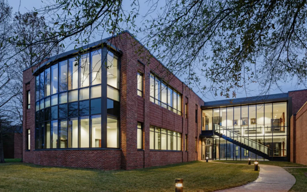 Modern red-brick law school building with large glass windows and a glass stairway entrance, illuminated at dusk and surrounded by trees and a curved walkway.