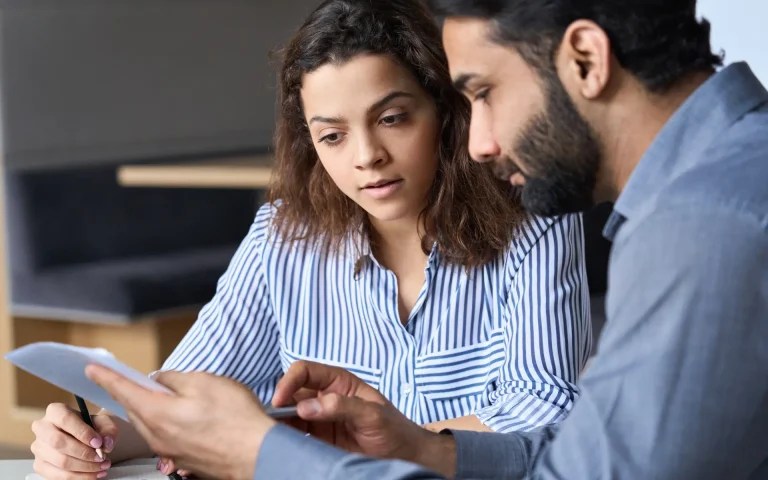 Two professionals reviewing a document together at a desk, discussing details while one points to the paper.