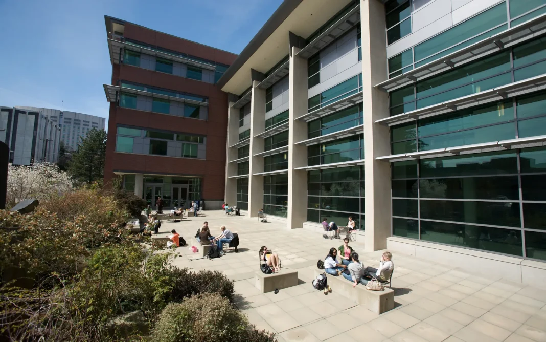 Modern Seattle University campus building with large glass windows and a courtyard where students are sitting and studying outdoors on a sunny day.