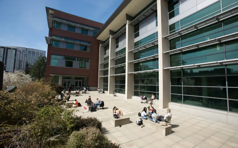Modern Seattle University campus building with large glass windows and a courtyard where students are sitting and studying outdoors on a sunny day.