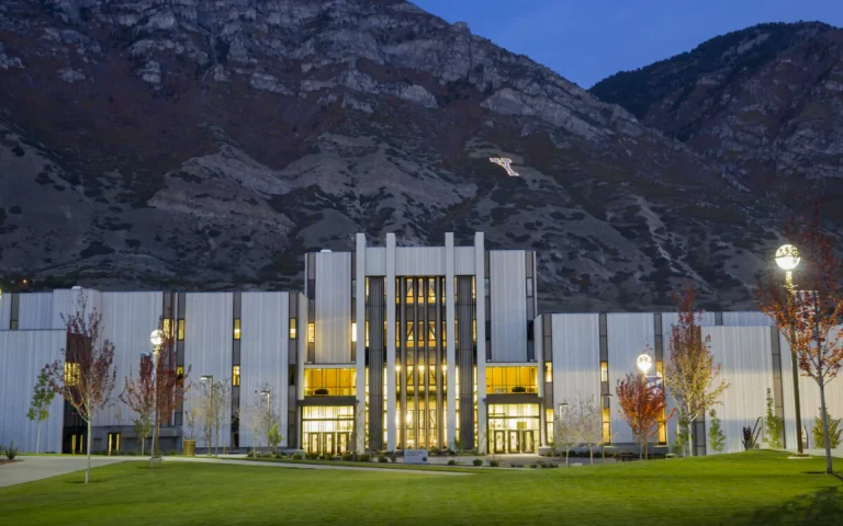 Brigham Young University’s law school building illuminated at dusk with the mountains behind it and the large white “Y” visible on the hillside.