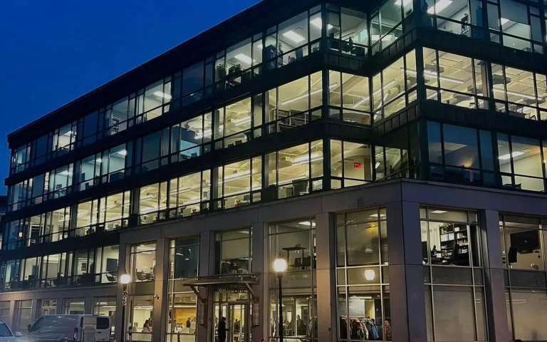 Modern glass-front academic building at night with brightly lit classrooms and offices visible through large windows, identified as the Maine Law building.