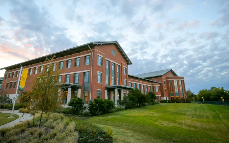 Red brick Baylor Law School building on a landscaped campus lawn under a cloudy evening sky.