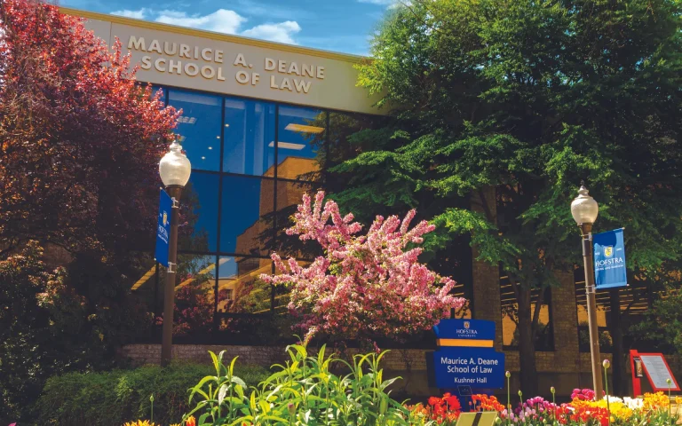 Exterior of the Maurice A. Deane School of Law building at Hofstra University, surrounded by colorful flowers and trees in bloom.
