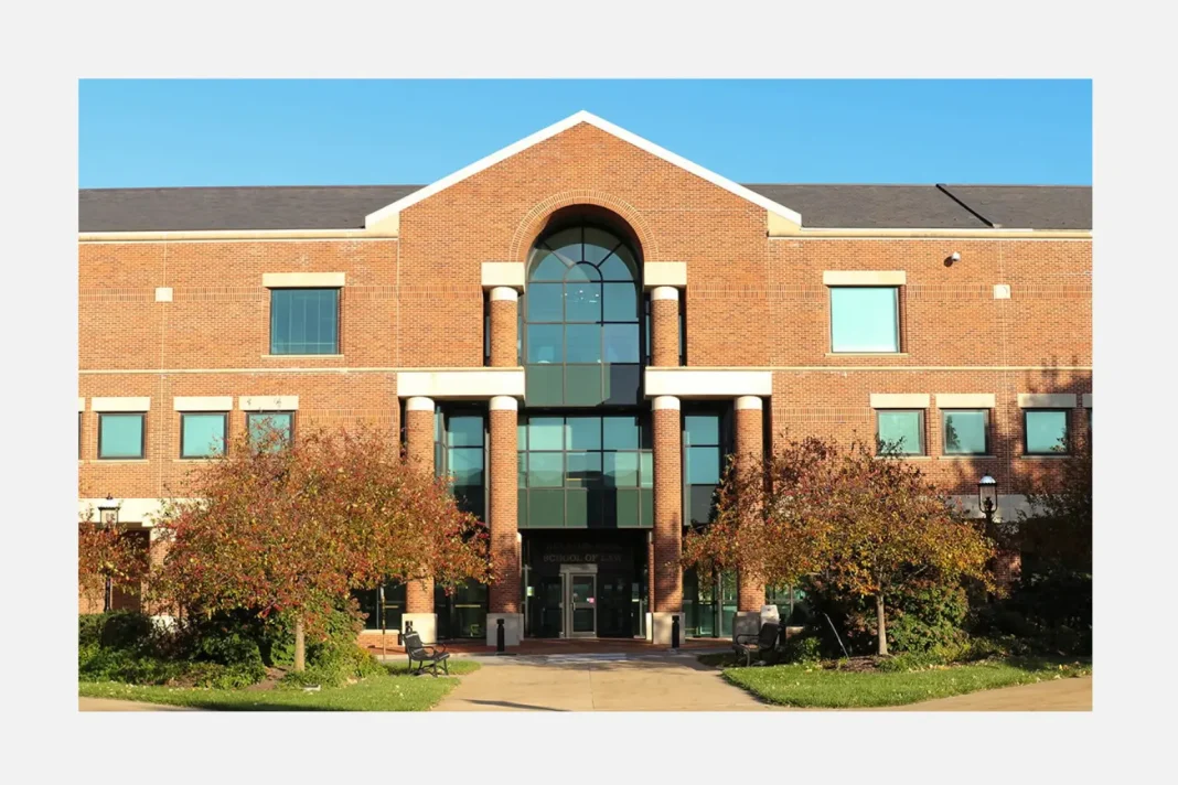 Red brick University of Missouri School of Law building with a central arched glass entrance and trees lining the walkway in front.