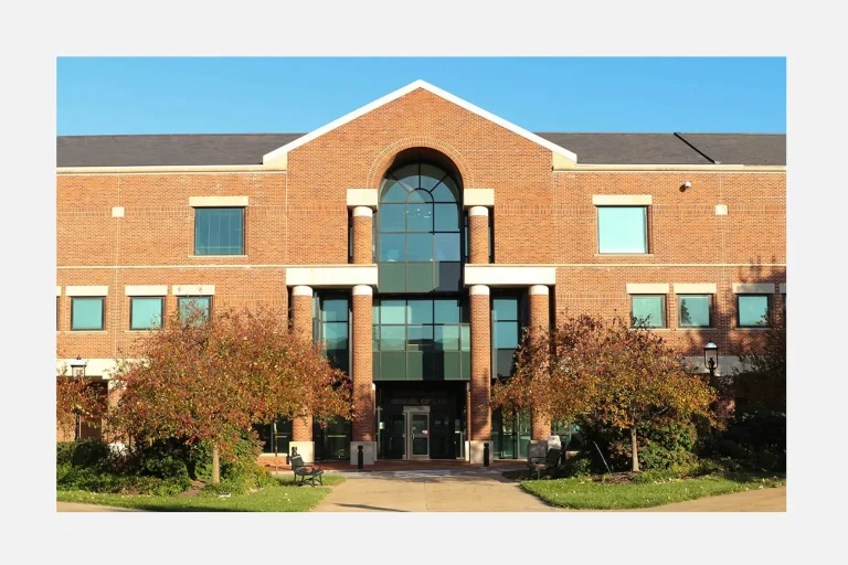 Red brick University of Missouri School of Law building with a central arched glass entrance and trees lining the walkway in front.