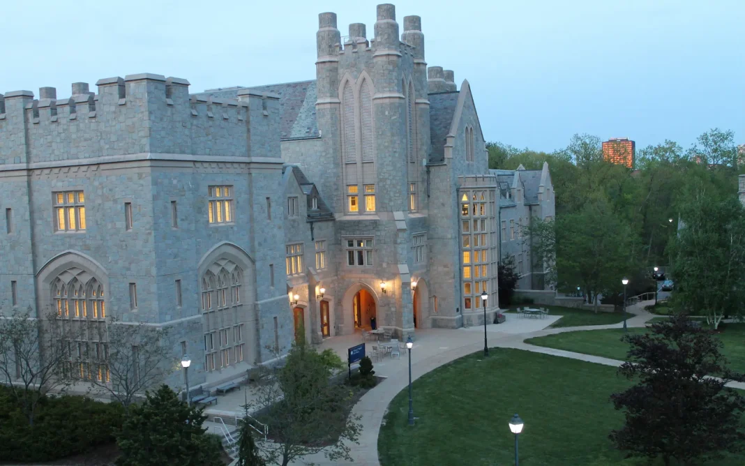 Historic stone law school building at the University of Connecticut campus at dusk, with illuminated windows, arched entrances, and a landscaped courtyard with walkways and lampposts.