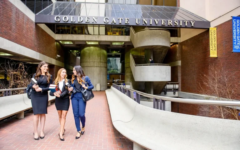 Three students in business attire walking and talking while carrying books outside the entrance of Golden Gate University.